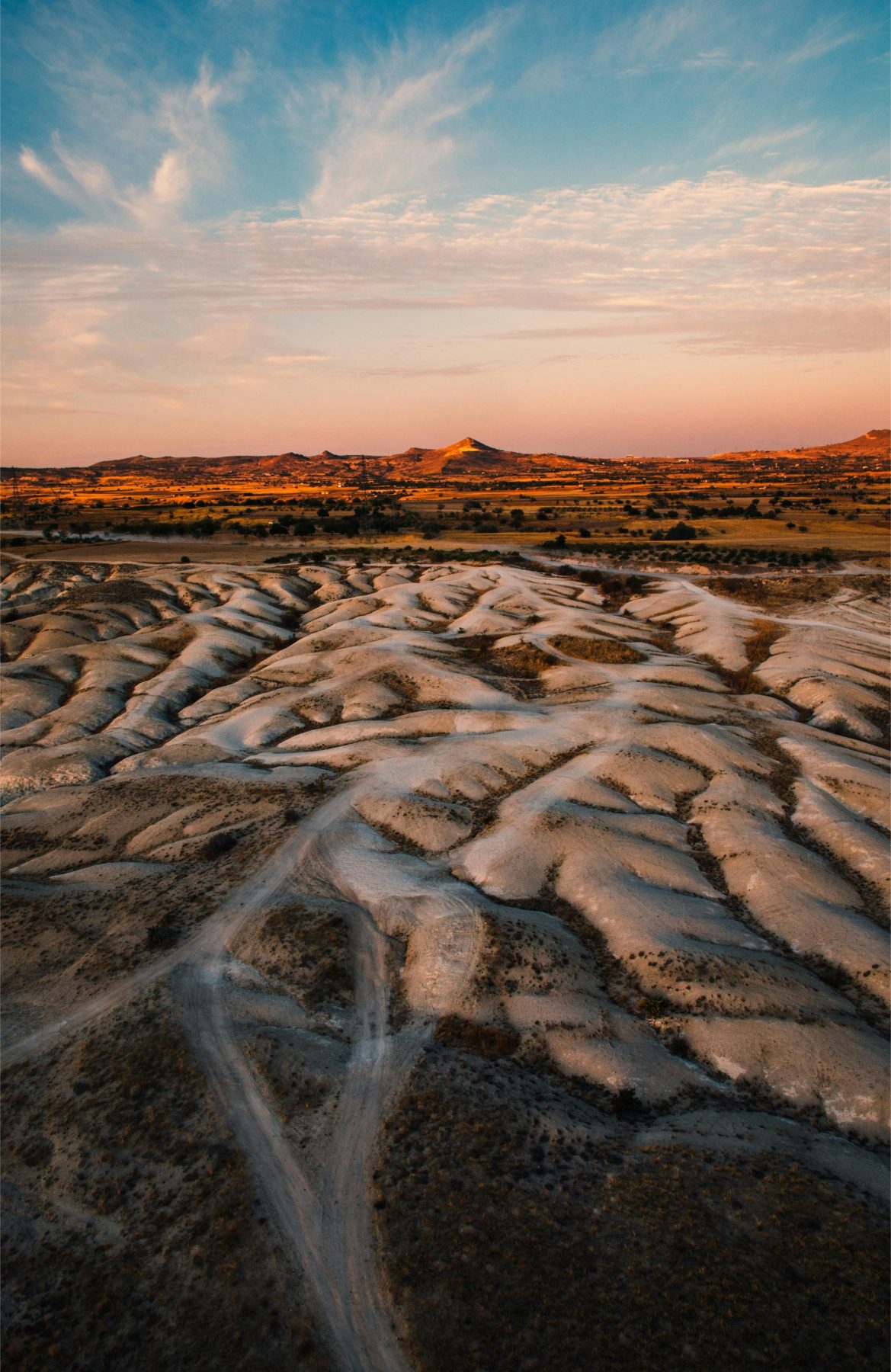 Een zanderig landschap in Cappadocië met op de achtergrond een oranje lucht en heuvels.